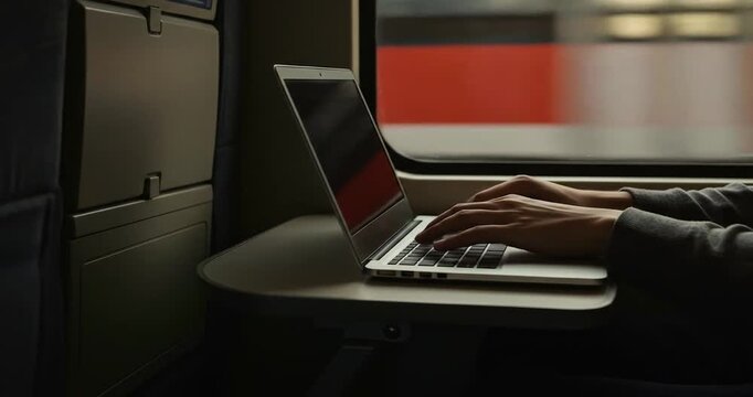 Person working on laptop in train during sunset