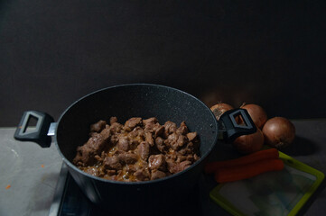 Cooking pot with meat, onions, and cutting board with knife and carrots