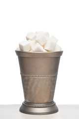 A silver cup filled with white sugar cubes on a white background.