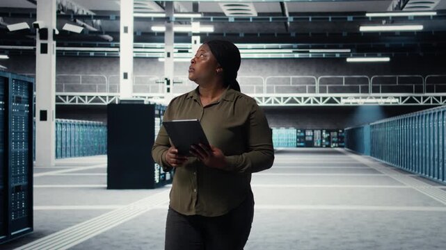 Engineer with tablet walks through data center server rows, implementing advanced power management solutions. IT professional using device to oversee server hub, reducing energy consumption, camera A