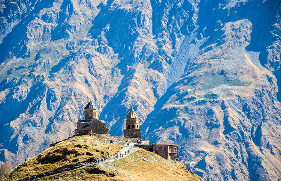 Medieval Georgian Orthodox Gergeti Trinity Church stands on a rugged hill Steep, rocky the Greater Caucasus mountains loom behind it. Georgia