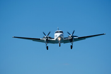 Small propeller plane flying in the blue sky on a sunny day. Twin-engine plane soaring through a clear blue sky.