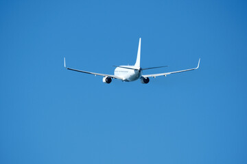 The plane that's just taken off drifts away from the airport across clear blue sky. Airplane flying in the blue sky on a sunny day. Airplane taking off, rear view. Travel concept.