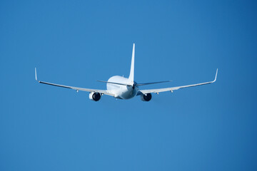 The plane that's just taken off drifts away from the airport across clear blue sky. Airplane flying in the blue sky on a sunny day. Airplane taking off, rear view. Travel concept.