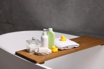Baby accessories and bathing products on wooden tray in bathtub indoors, closeup