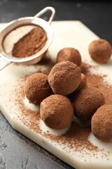 Tasty chocolate candies with cocoa powder on black table, closeup