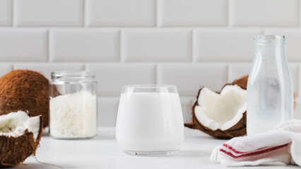 Fresh coconut milk in glass with whole and halved coconuts. Vegan healthy breakfast
