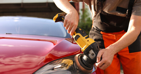 Man polishing car headlight with orbital polisher outdoors, closeup