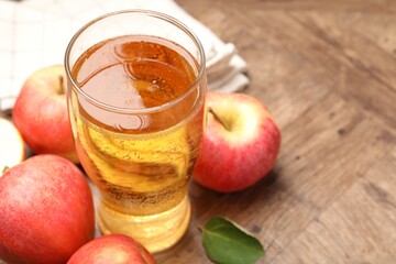 Fresh cider in glass and apples on wooden table, closeup. Space for text