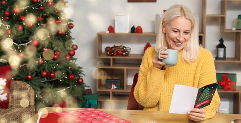 Mature woman with coffee cup reading greeting card for Christmas celebration at home