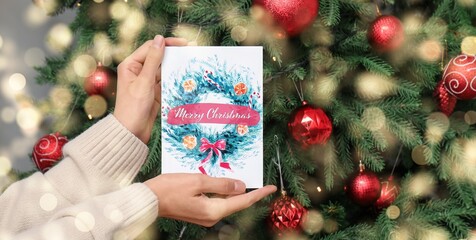 Woman holding greeting card near decorated Christmas tree