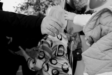 Black and white photo of a baby reaching for a ribbon held by an adult, symbolizing connection, family love, childhood innocence, and generational bond in a timeless candid moment.