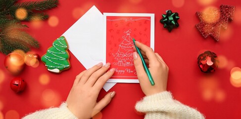 Female hands with greeting card, pen and beautiful Christmas decorations on red background, closeup