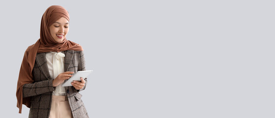 Young Muslim businesswoman using tablet computer on light background
