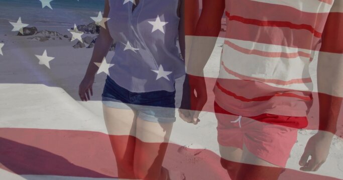 Walking couple wearing striped trunks and light blouse, shorts on sandy beach, with US flag overlay