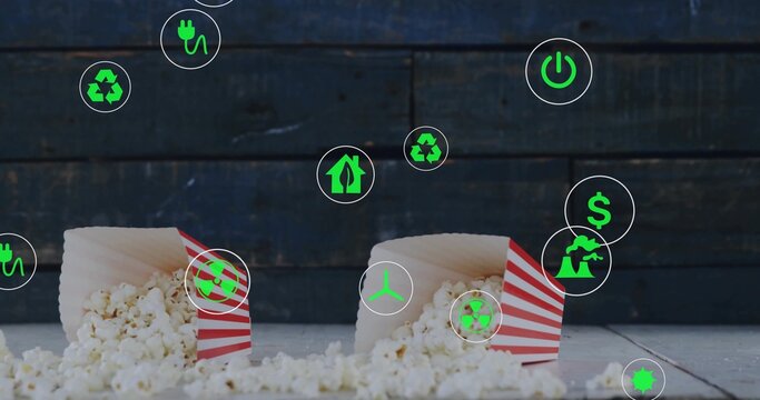 Spilling popcorn from red-and-white-striped boxes on tabletop showing green energy recycling icons