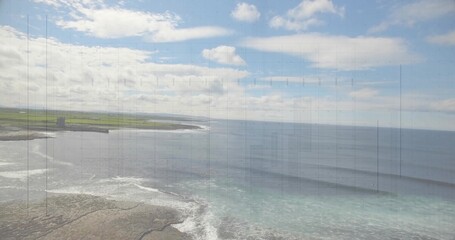 Featuring rocky shoreline, waves crashing against stones by green fields, with tower ruin