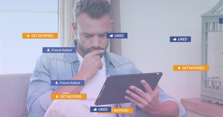 Mid-adult man holding tablet on couch at home, with floating notification icons and birdcage