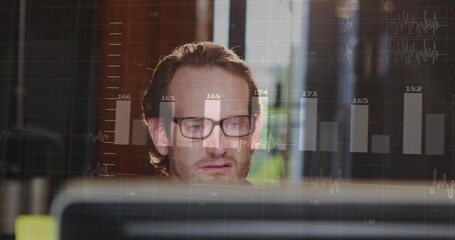 Man in eyeglasses analyzing data on monitor at office desk, with bar and line graphs overlay