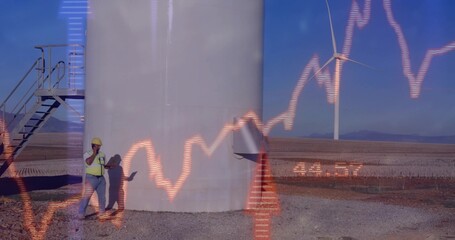 Wind farm technician with helmet reviewing graph and talking on phone at turbine base, copy space