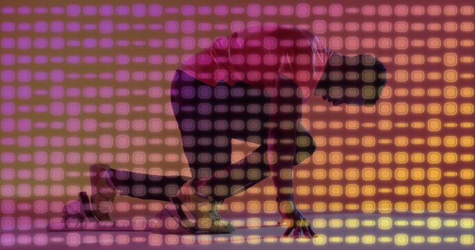 Crouching athlete in red shirt and spikes initiating sprint at studio with gradient grid backdrop