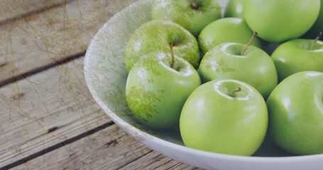 Displaying white ceramic bowl holding shiny green apples on wooden kitchen table, copy space