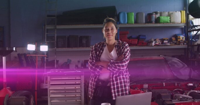 Standing technician in red plaid shirt crossing arms in auto workshop, with laptop and car hood