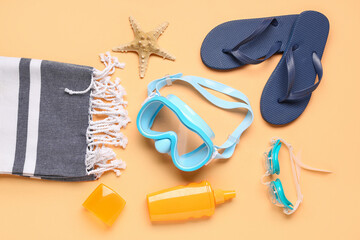 Swimming mask, goggles, flip flops, blanket and bottle of sunscreen on beige background