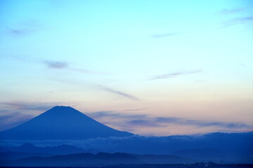 夕暮れ時の空がグラデーションで青色からピンク色に染まり、遠くに富士山のシルエットが浮かぶ幻想的な風景写真。