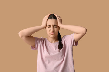 Beautiful young woman suffering from headache on beige background