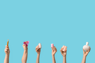 Female hands with herbal massage bag, soap bar, candle, face massage tool, flower and bottle of sea salt on blue background