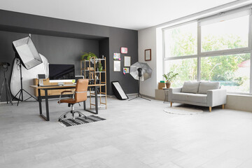 Photographer workplace with computer, grey sofa and lighting equipment in modern photo studio