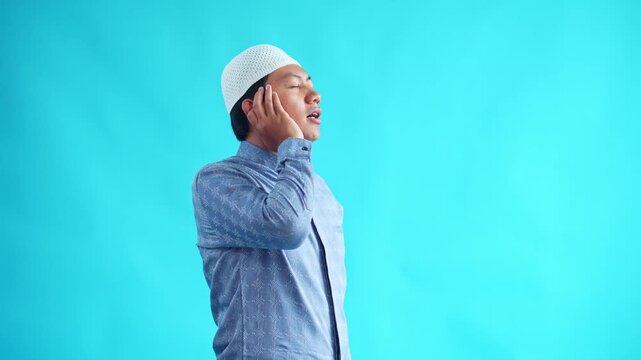 Muslim man doing adzan with serene expression feeling spiritual connection isolated on blue background
