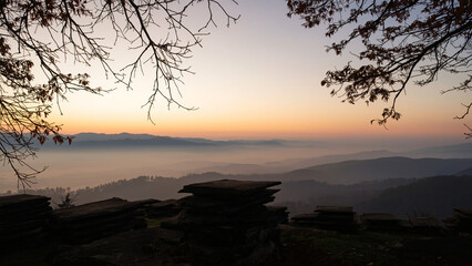 Gray stone slab with round top on mossy cliff edge. Overlooks valley with lush green vegetation, mountains shrouded in dense fog. Natural landscape, serene atmosphere, perfect for product placement.