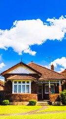 Fototapeta premium Charming single-story suburban house with a red roof and white picket fence under sunny skies. 