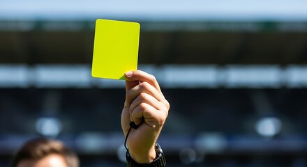 Person Holding Bright Yellow Card in Stadium with Blurred Background