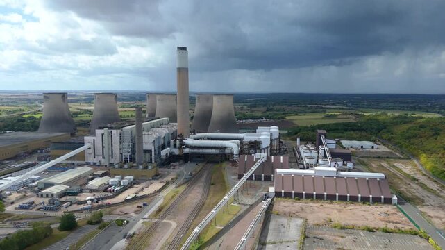 Aerial cinematic drone close up view of cooling towers and smoke stacks at energy power plant storm thunder skies England UK