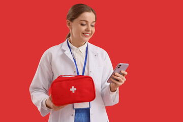 Female doctor with first aid kit and mobile phone on red background