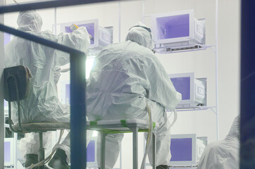 Workers in protective gear engage in powder coating process inside a clean room environment, ensuring precise application on equipment components