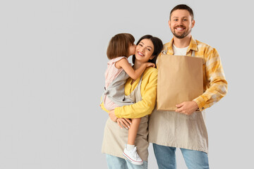 Happy family in aprons with paper bag of food on light background