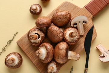 Wooden board with fresh raw mushrooms and thyme on yellow background