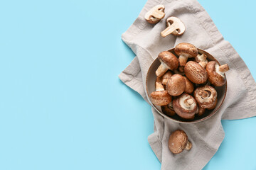 Bowl with fresh raw mushrooms on blue background