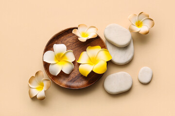 Wooden plate with beautiful plumeria flowers and stones on beige background