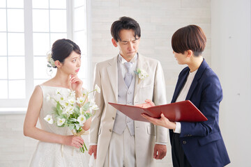 悩みながら打ち合わせする結婚式の司会者と新郎新婦
