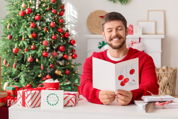 Young man reading Christmas greeting card at home