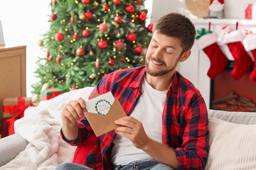 Young man with Christmas greeting card on sofa at home