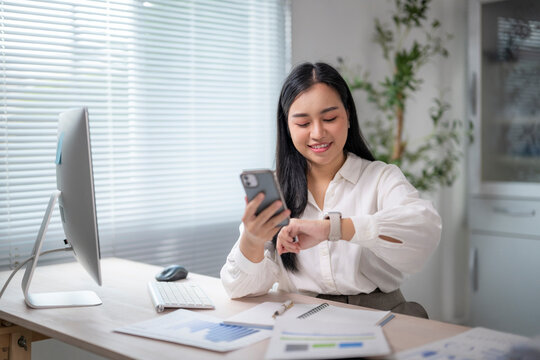 Businesswoman using smartwatch and smartphone at office desk - Powered by Adobe