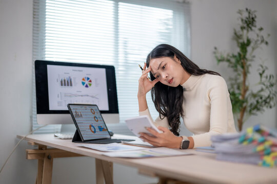 Stressed asian accountant working with calculator and charts at office desk