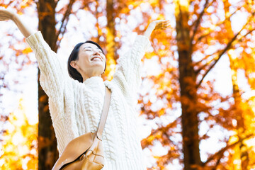 紅葉した森の中で腕を伸ばしている女性　ライフスタイルイメージ