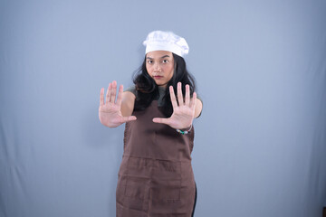 A young woman chef, wearing an apron and hat, makes a clear "stop" gesture